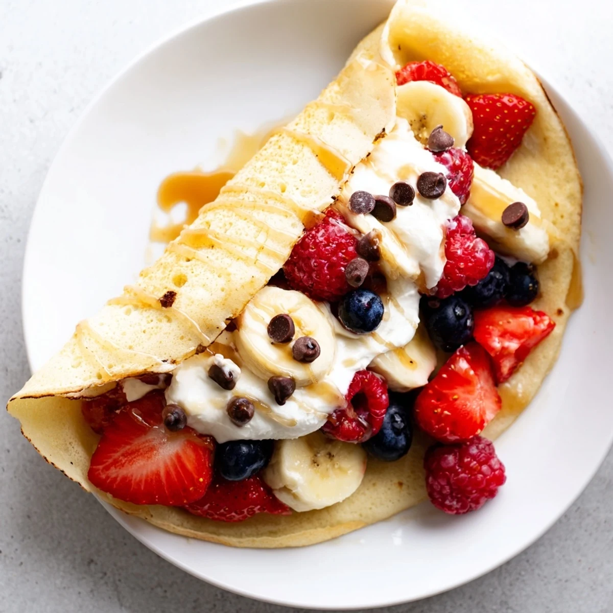 Golden pancake tacos stuffed with fresh berries and drizzled maple syrup on a plate