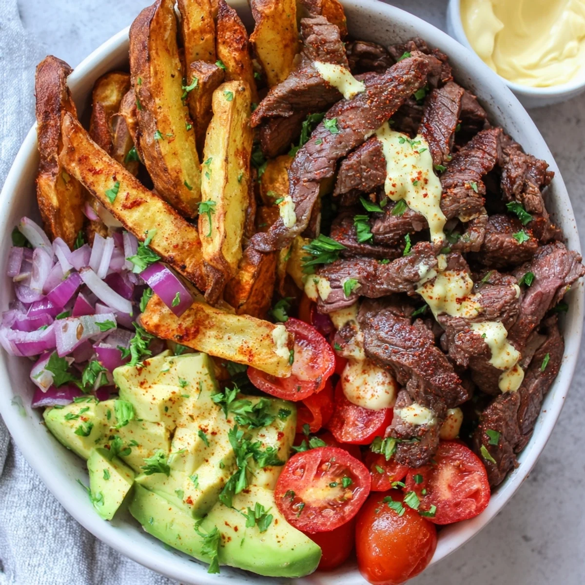 Golden French fries topped with juicy sliced steak, fresh avocado, and vibrant cherry tomatoes.