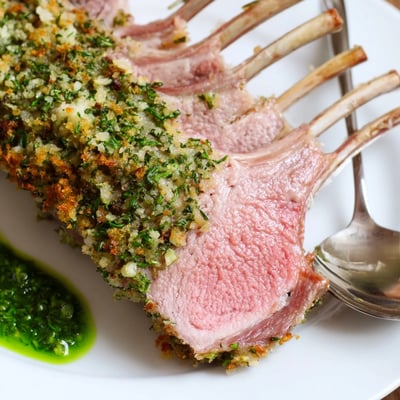 Close-up of succulent Garlic Herb Roasted Rack of Lamb with Mint Sauce, highlighting a fragrant garlic-herb crust and drizzle of vibrant homemade mint sauce.
