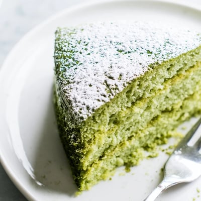Fluffy matcha cake with a vibrant green crumb served alongside a cup of tea